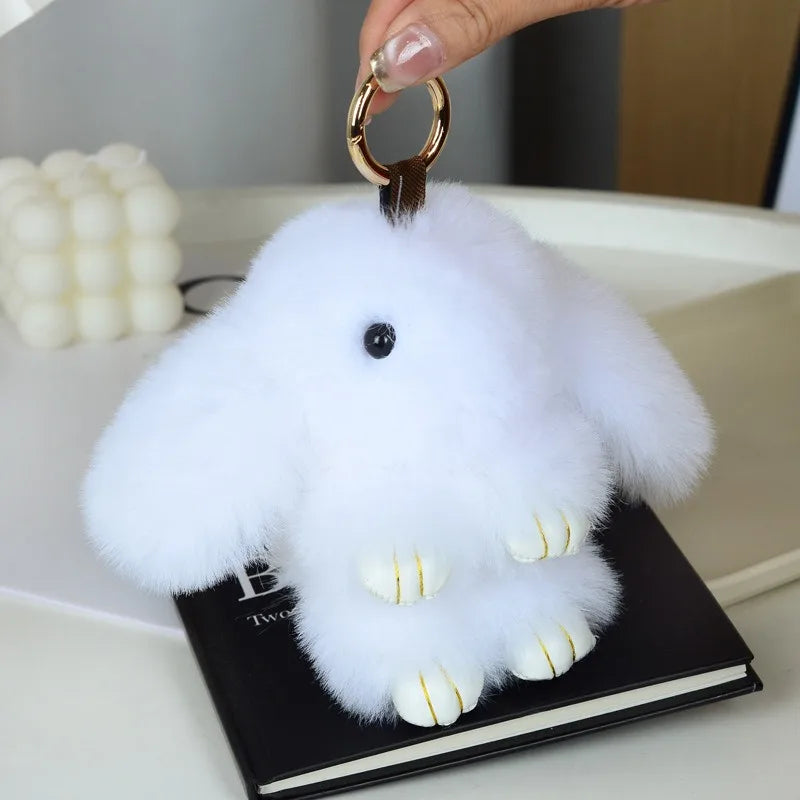 A white fluffy angel bunny keychain with a pom pom tail is displayed on a black book.