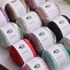 A collection of glitter yarn spools in various shades including pink, silver, and green, packaged for knitting and crafting.
