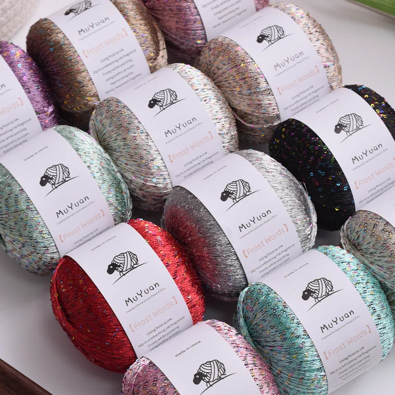 A collection of glitter yarn spools in various shades including pink, silver, and green, ready for knitting and crafting.