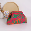 A hand-knit clutch bag featuring vibrant pink, orange, and green geometric patterns with pearl accents resting on a white sur
