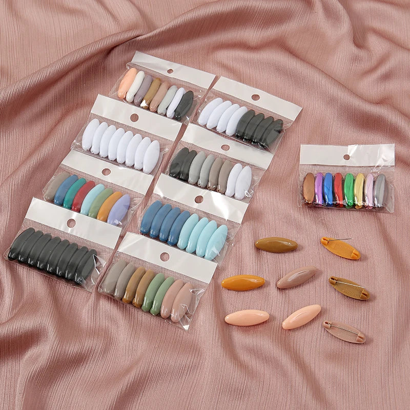 A set of eight solid color scarf pins in various shades of beige, gray, and white are displayed in small clear plastic bags o