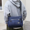 A person is holding a navy blue men's business crossbody bag with multi-layered pockets against a light background.