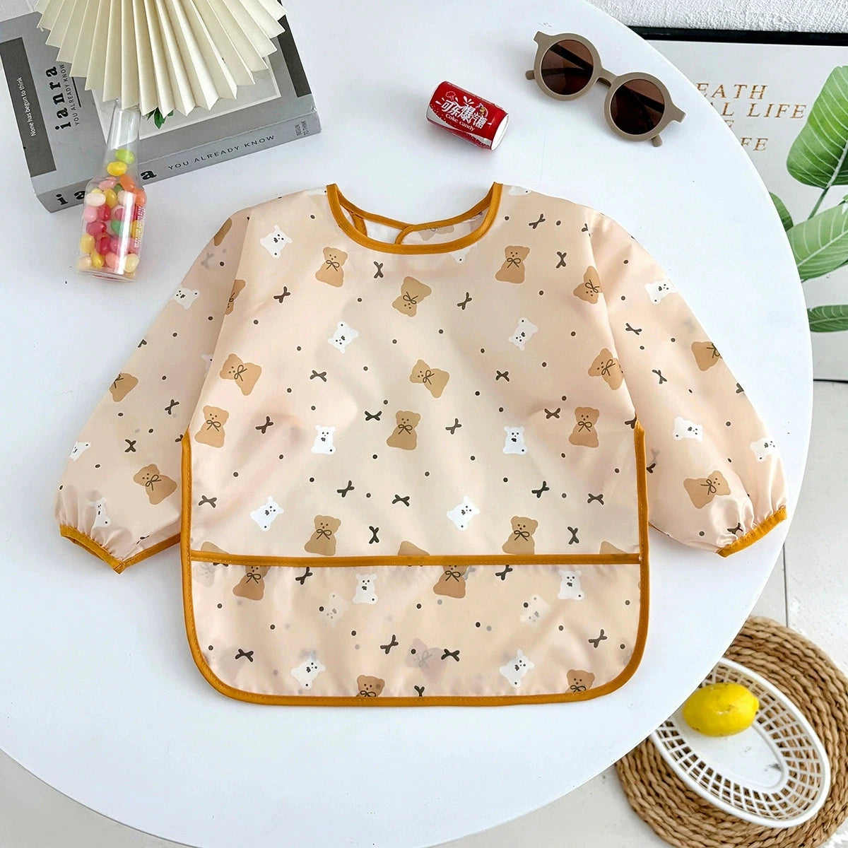 A light peach waterproof long-sleeve baby feeding smock with a pattern of small bear and cat motifs.