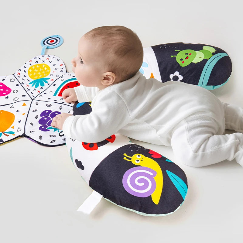 A baby is lying on a high contrast tummy time pillow featuring colorful animals and shapes.