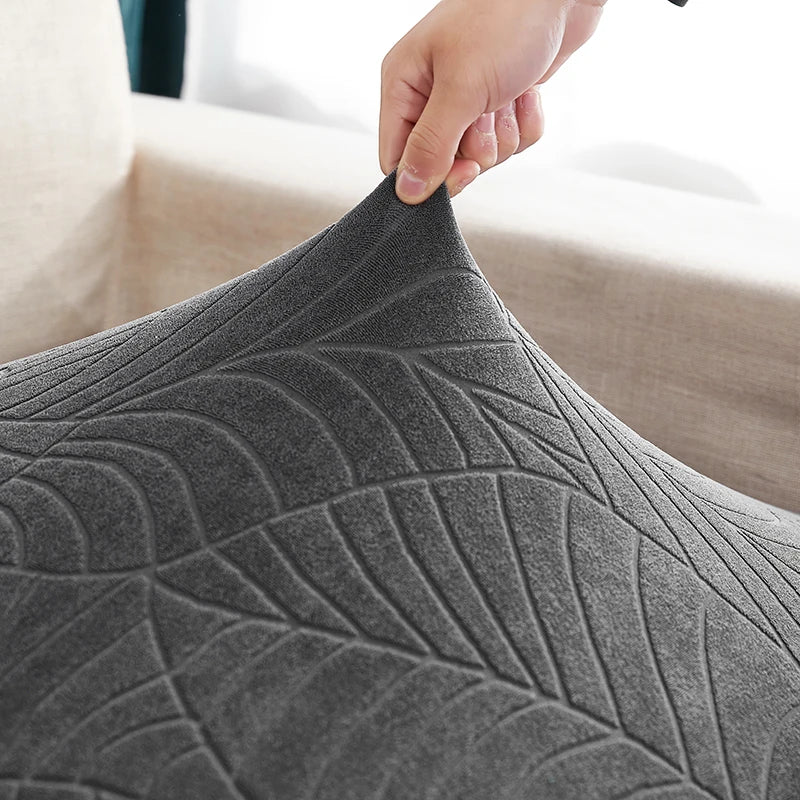 A hand is adjusting a gray stretch jacquard sofa cover with an anti-slip backing.