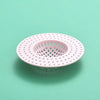 A pink silicone sink drain filter strainer with a perforated design is shown on a light green surface.