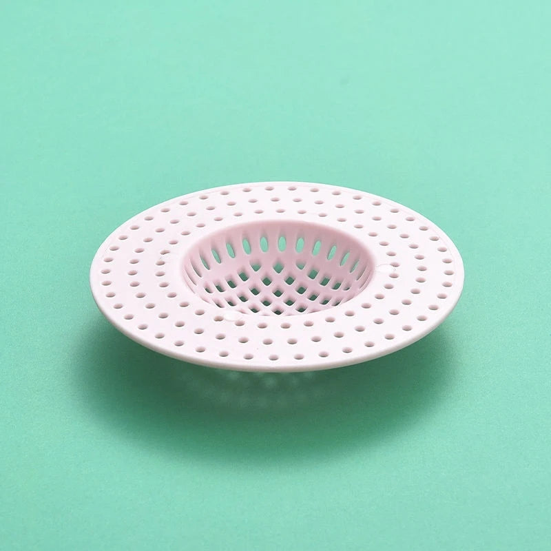 A pink silicone sink drain filter strainer with a perforated design is shown on a light green surface.
