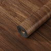 Roll of self-adhesive wood grain floor stickers or peel-and-stick wallpaper on a wooden surface.