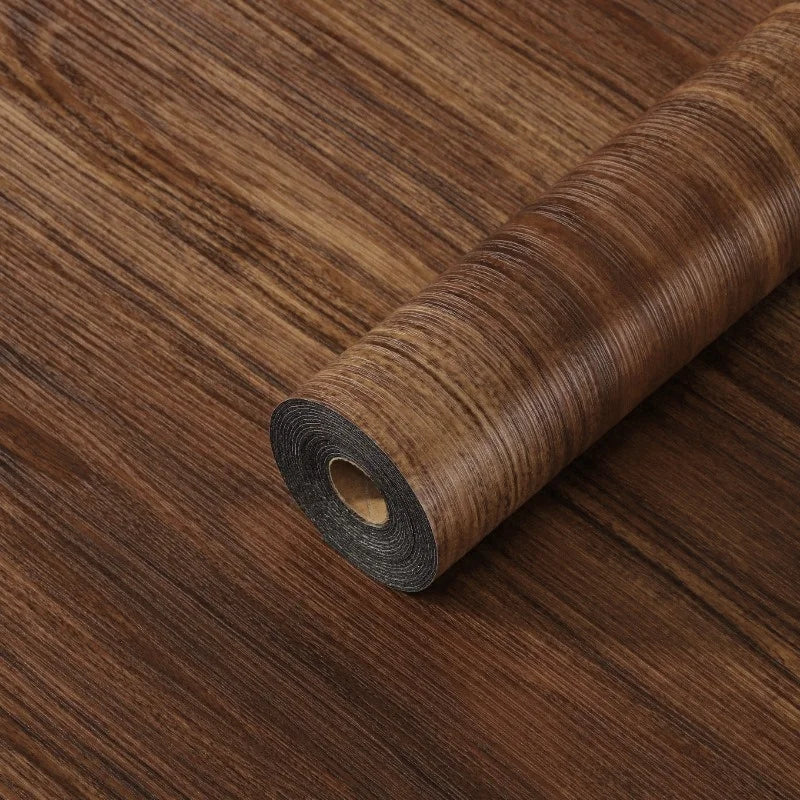 Roll of self-adhesive wood grain floor stickers or peel-and-stick wallpaper on a wooden surface.