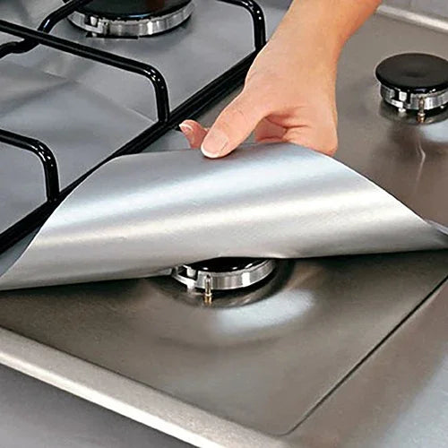 A hand places a silver silicone liner onto a gas hob surface.