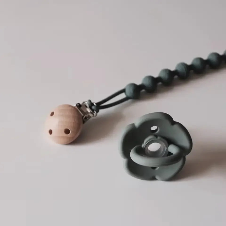 A silicone pacifier clip with a teether is shown against a light background.