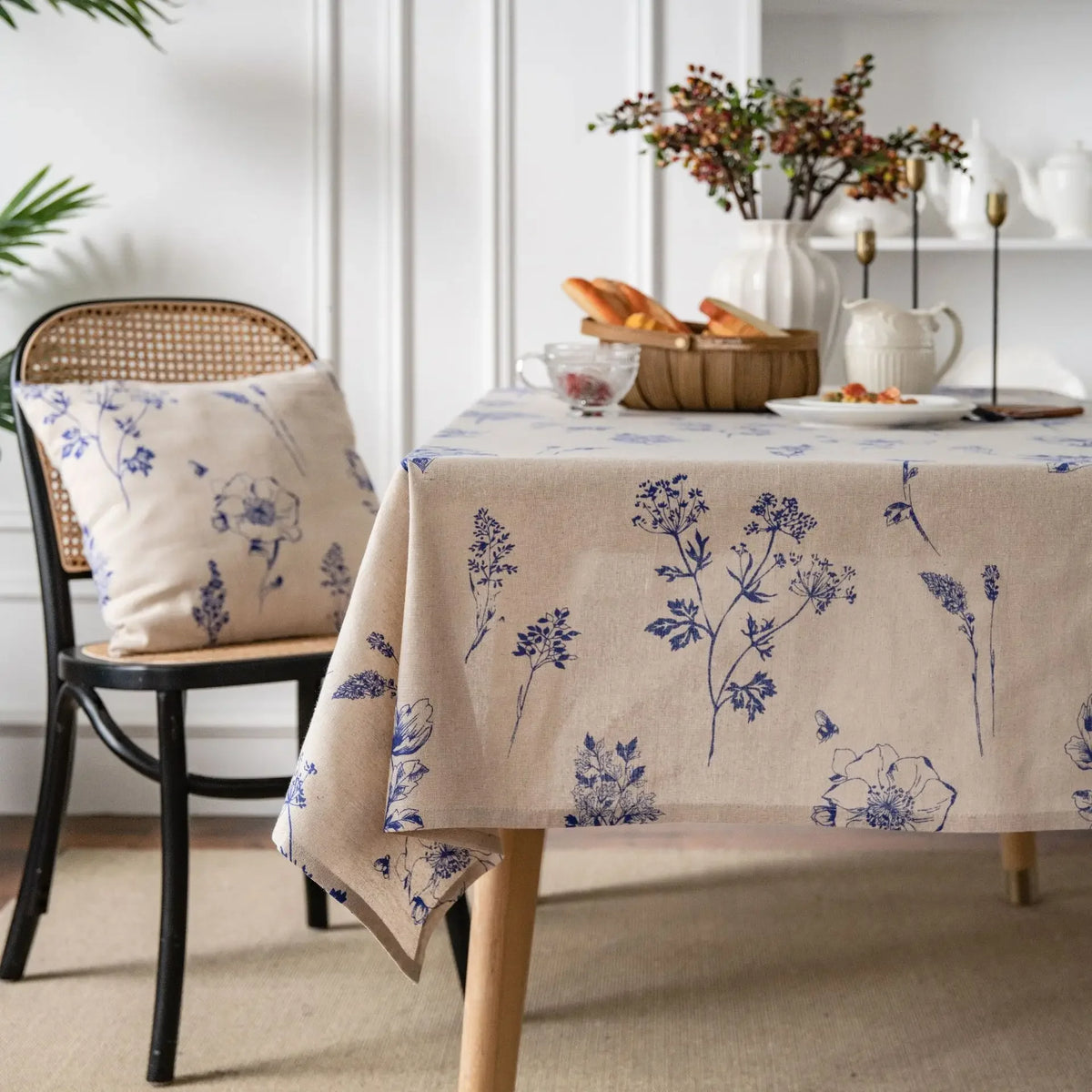 A beige cotton-linen tablecloth with a blue rustic fern print is set on a wooden table.