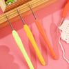 A set of four precision crochet hooks in yellow and orange with comfort grips resting on a pink surface.