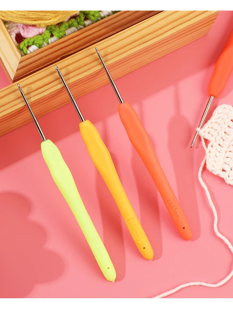 A set of four precision crochet hooks in yellow and orange with comfort grips resting on a pink surface.