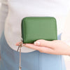 A hand holds a green accordion wallet with a silver chain attached, against a light background.