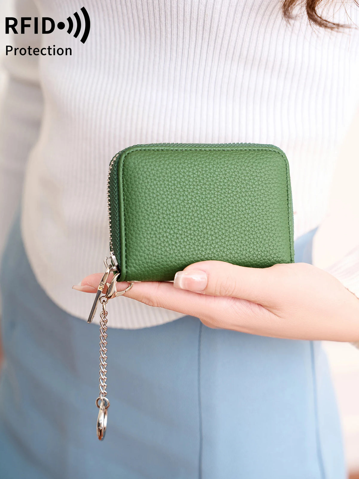 A hand holds a green accordion wallet with a silver chain attached, against a light background.