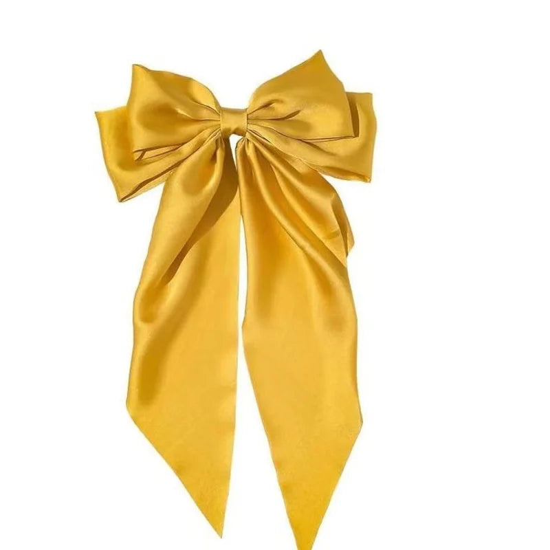 A golden yellow silk bow used as a hair accessory or ponytail holder.
