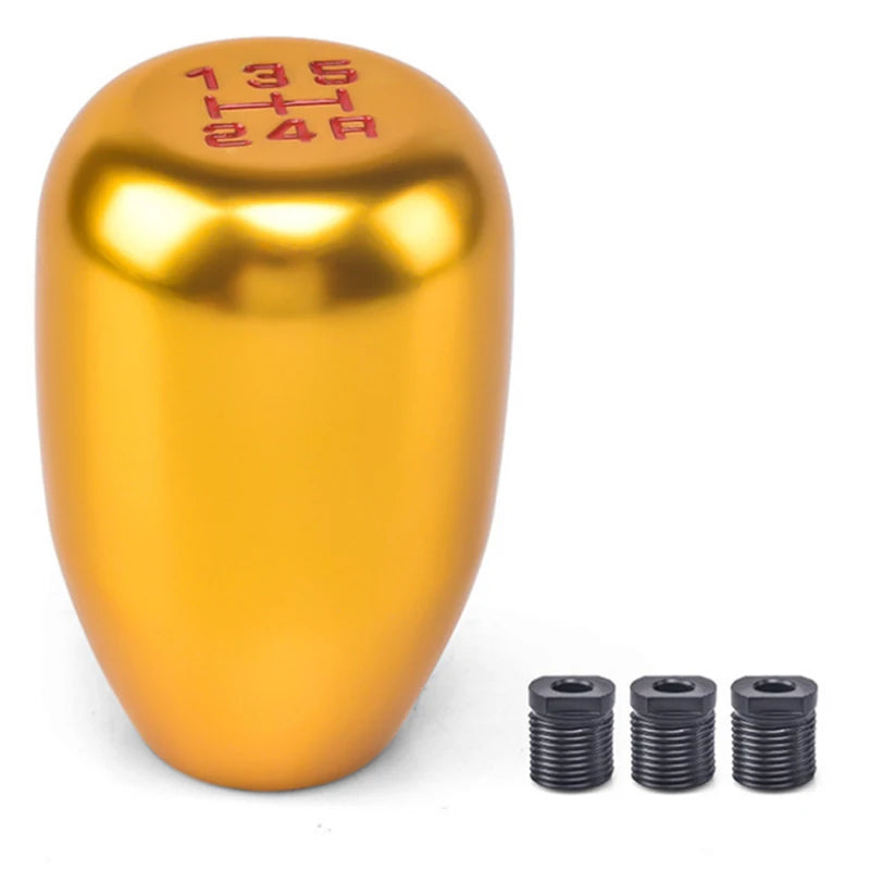 A shiny gold aluminum gear shift knob with markings and three separate adapters.