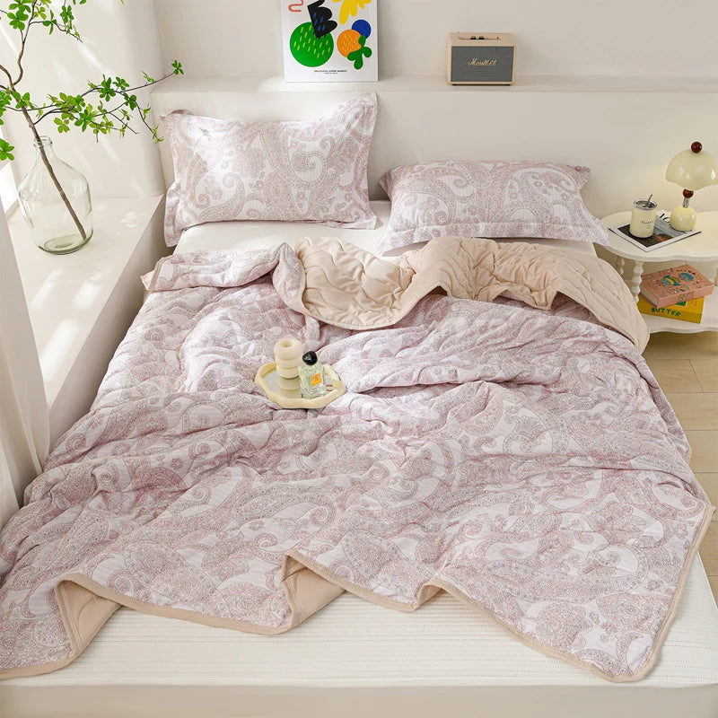 A soft pink quilted blanket is displayed on a white shelf with pillows and decorative items.