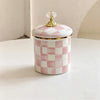 A white and pink checkerboard porcelain storage jar with a gold lid sits on a white surface.