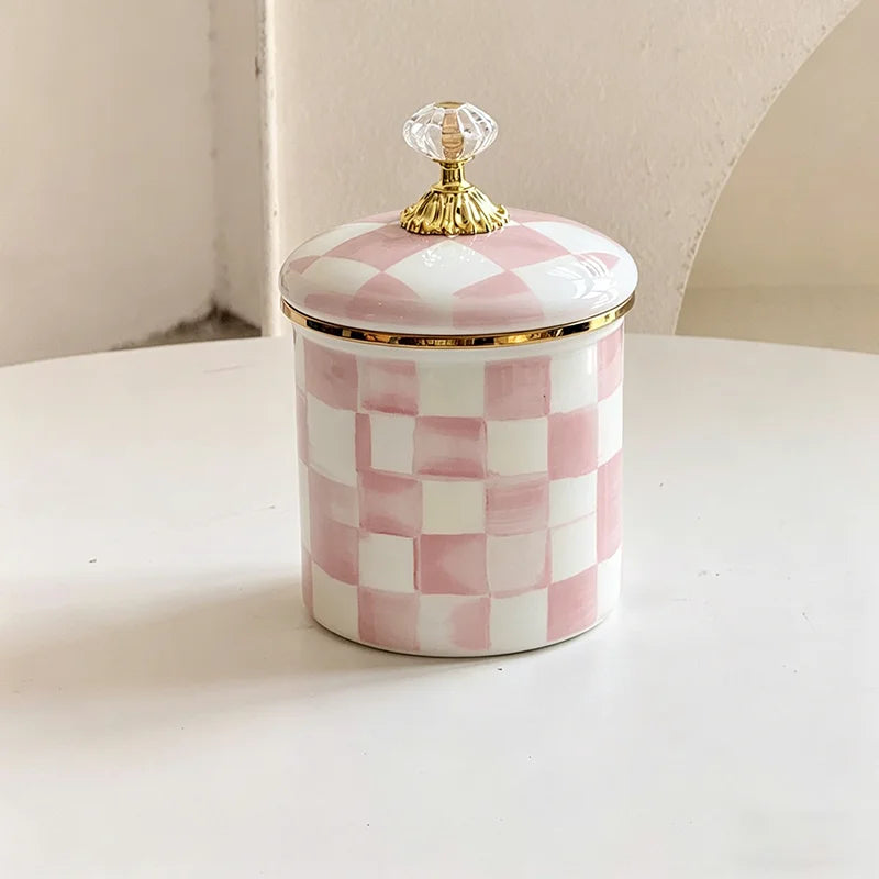 A white and pink checkerboard porcelain storage jar with a gold lid sits on a white surface.