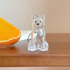 A clear glass pendant keychain shaped like a sitting fox or canine, resting on a wooden surface next to an orange slice.