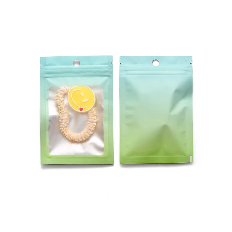 Two light green gradient resealable zipper pouches with clear windows, one containing a yellow necklace.