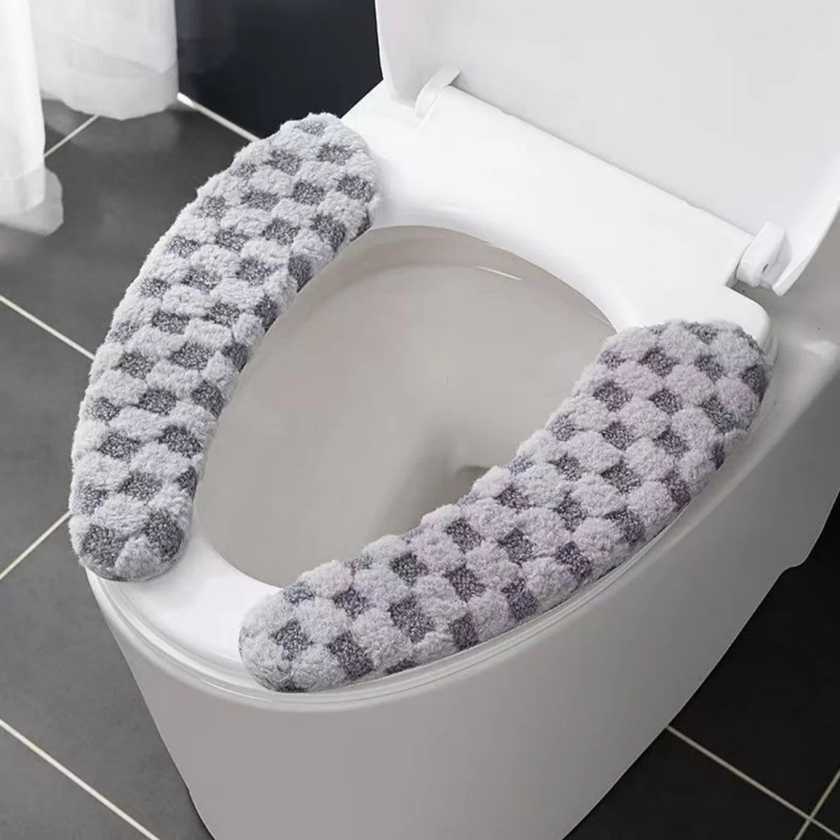 A plush winter toilet seat cushion cover with a gray and white patterned fabric is shown inside a white toilet bowl.