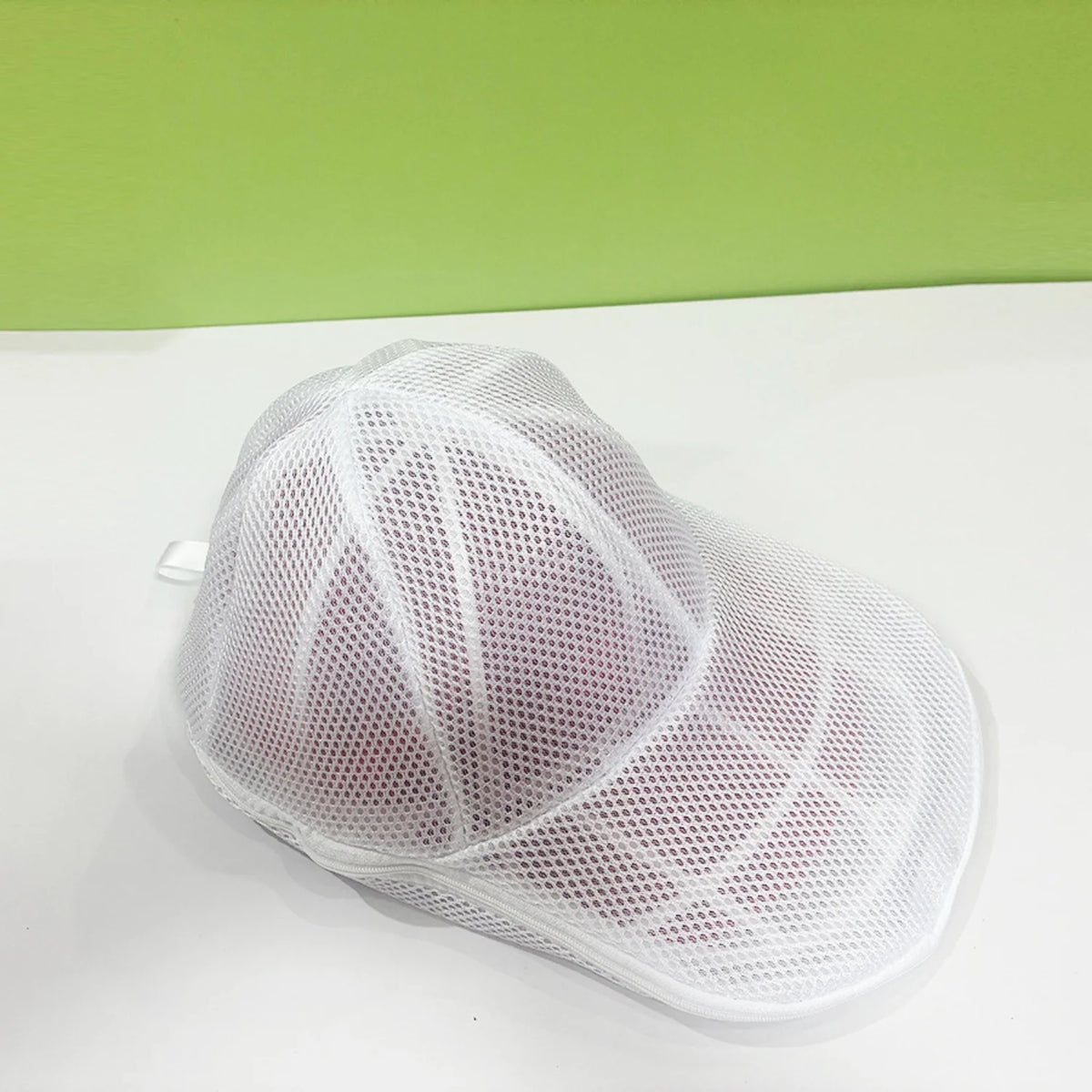 White mesh hat cleaning cage with a mesh bag resting on a white surface.
