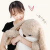 A person is hugging a large, light brown, long-eared rabbit plush toy.
