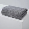 A folded gray textured bath towel with a chevron pattern resting on a white surface.