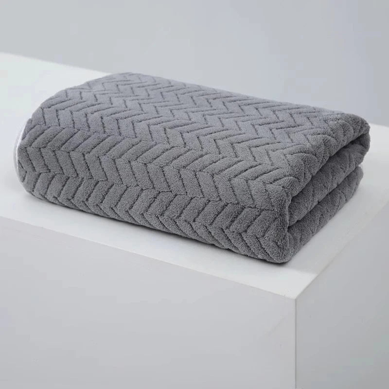 A folded gray textured bath towel with a chevron pattern resting on a white surface.