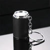 A black metal coin tube keychain with a silver chain and ring attached, shown on a reflective surface.