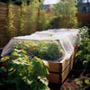 A raised garden bed covered with a fine mesh netting protecting young plants in a backyard setting.