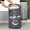 A gray drawstring laundry bag featuring a smiling face is being held by a person next to a silver suitcase.