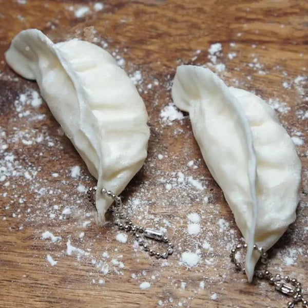 A white dumpling shaped squishy keychain rests on a wooden surface with scattered white powder.