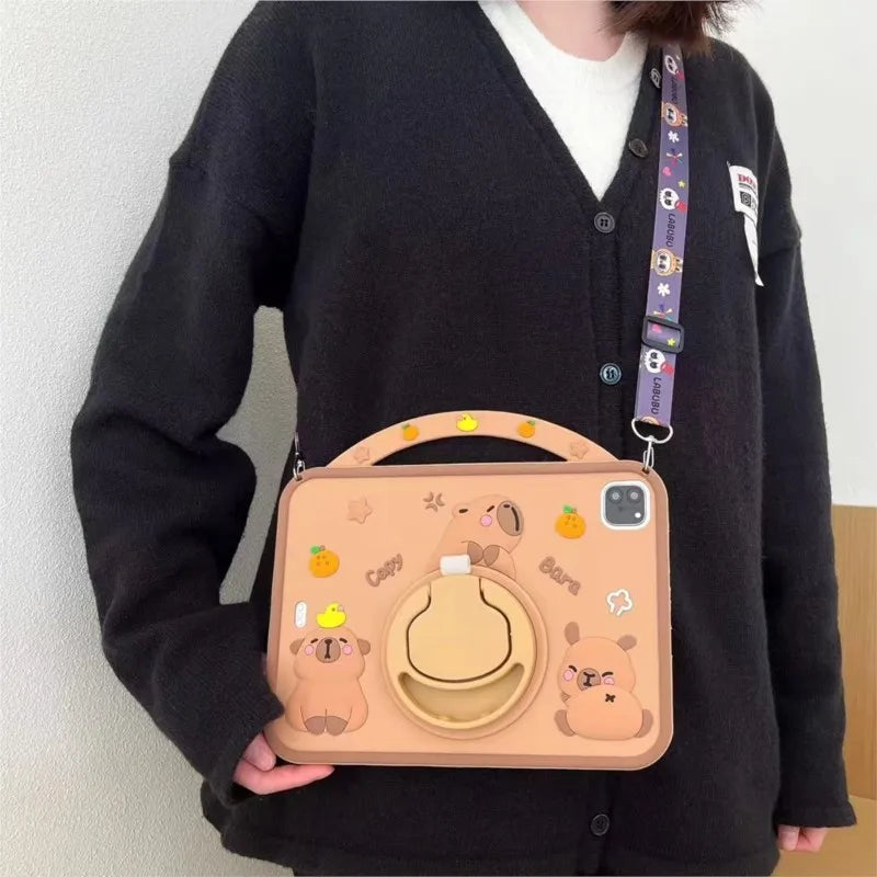 A light brown silicone case featuring a cute cartoon capybara design for an iPad, held by a person wearing a black cardigan.
