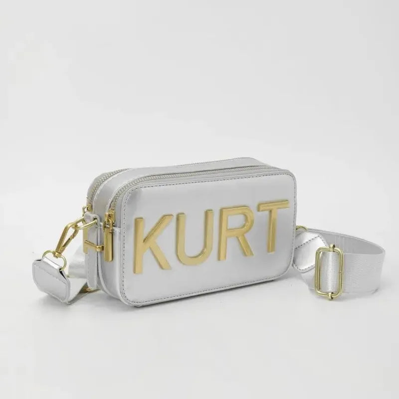 Silber-Ledertasche mit goldenen Lettern und weißem Riemen