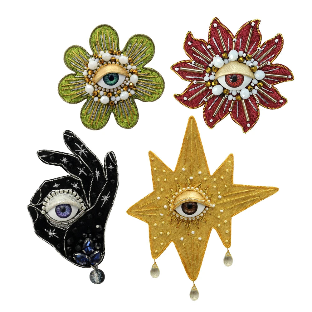 Three decorative patches featuring stylized eyes made of green, red, and gold rhinestones and beads.