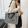 A woman holds a black and white striped canvas tote bag with inner pockets and a cream knit cardigan.