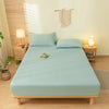 A light blue fitted bed sheet set with matching pillowcases is displayed on a wooden bed frame in a bright room.