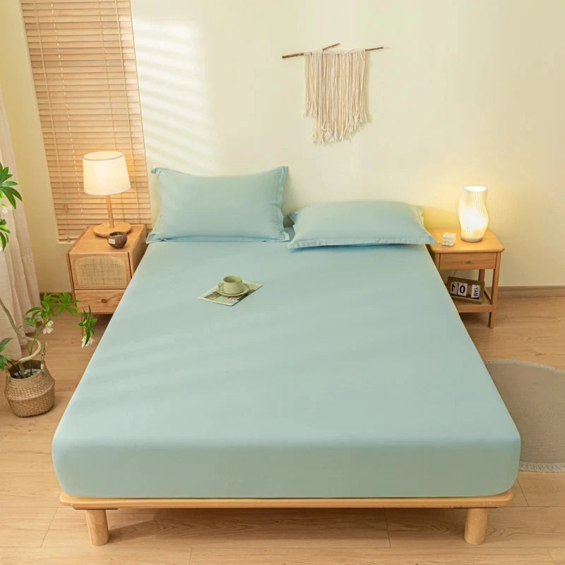 A light blue fitted bed sheet set with matching pillowcases is displayed on a wooden bed frame in a bright room.