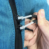 A hand is pulling a replacement zipper pull with a nylon cord out of a blue denim fabric.