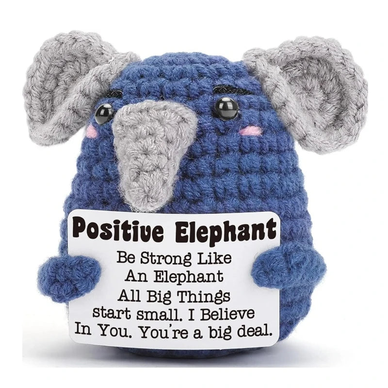 A handmade crochet elephant doll in blue and gray with a positive message card attached.