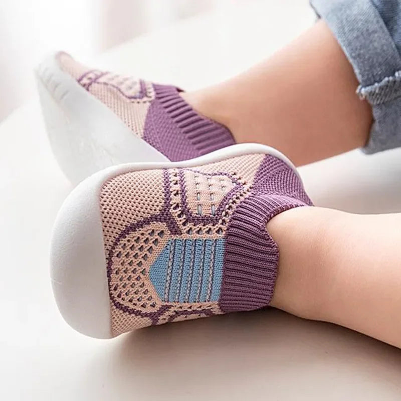 A close-up of a pair of purple and beige breathable soft-sole baby shoes with non-slip grip