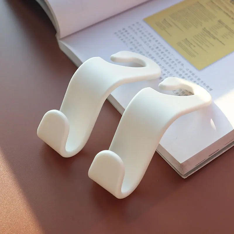 A pair of white universal car seat headrest hooks resting on a light-colored book.