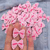 Pink and white embroidered fabric bows arranged on a denim background.