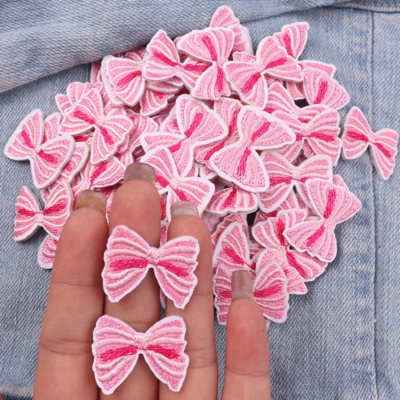 Pink and white embroidered fabric bows arranged on a denim background.