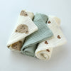 A stack of soft cotton gauze burp cloths with brown bear designs in cream and sage green colors.