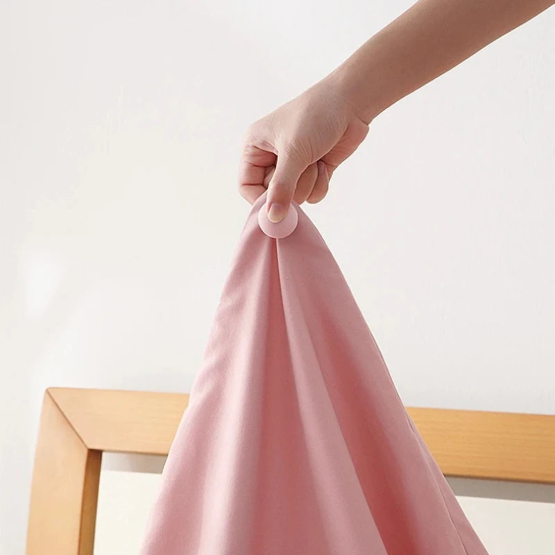 A hand is using a round clip to fasten a pink anti-slip bedsheet quilt.